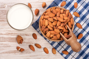 Almond milk in a glass and almonds in a bowl on light wooden background. Top view