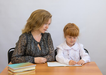 Little girl with her mother writes at the table with exercise books and textbooks