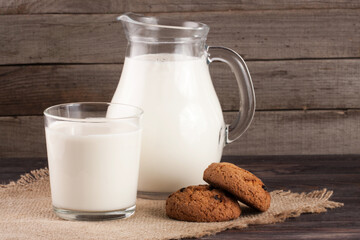 jug and glass of milk with oatmeal cookies on a wooden background