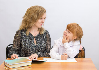 Fototapeta premium The little girl at the table with exercise books and textbooks, looking at mother