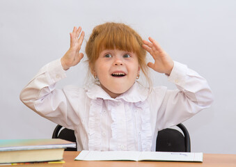 Little girl at the desk, surprised eyes widened, raising his hands to his head