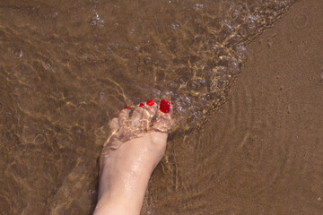 Feet of woman with nails painted red on the sand of the sea