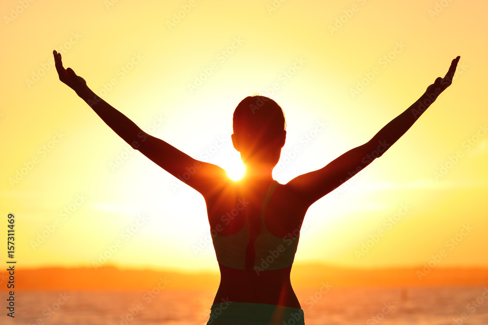 Wall mural Freedom woman with open arms silhouette in sunrise against sun flare. Morning yoga girl practicing sun salutation outdoors. Carefree person living a free life. Success freedom happy life concept.