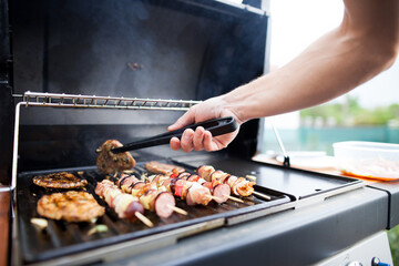 Young man grills some kind of marinated meat and vegetable on gas grill during summer time