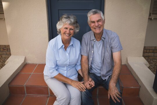 Portrait of smiling senior couple sitting together against house