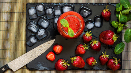 Obraz na płótnie Canvas Top view strawberry smoothie with fresh berries and ice on a black stone board