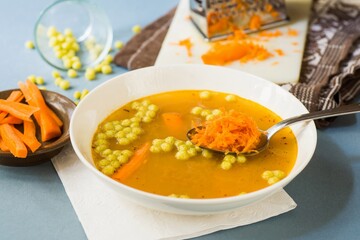 Vegetable soup with grated raw carrot on spoon.