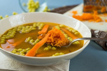 Vegetable soup, sliced and grated carrot, pea pearl, white plate, spoon.