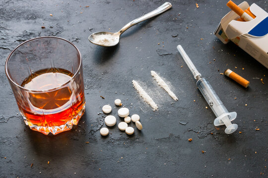 Alcohol in a glass, drugs, syringe, pack of cigarettes on a black background. Concept of bad habits