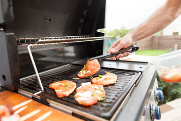 Hand of young man grilling some meat and vegetable-meat skewers on huge gas grill (Shallow DOF)