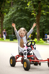 Little cheerful smiling girl driving race car in the park