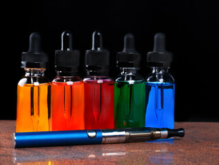Electronic cigarette and bottles with vape liquid on granite surface and black background