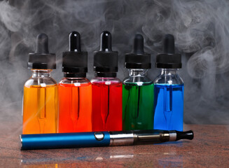 Electronic cigarette and vape liquids within vapor on granite surface and black background