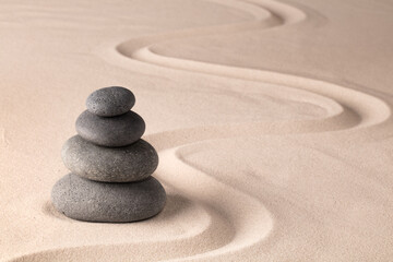 balancing a stack of black hot stones for spa wellness therapy. Zen meditation rock andsand garden. A yoga background.