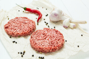 Two raw hamburgers made from organic meat on a white wooden background with spices.