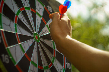outdoor darts game with man hand and blurry green background