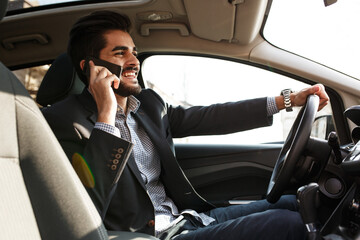 Handsome businessman talking on the phone while driving  car unsecured without fastening seat...