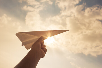 Taking flight! hand holding paper airplane in the sky.  - Powered by Adobe