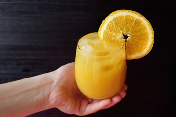 Orange juice in hand on dark background 