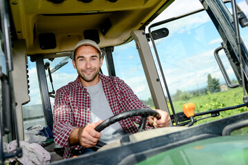 Fototapeta premium handsome young male farmer driving his tractor during harvest in the field countryside