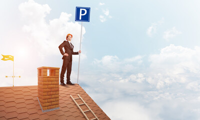 Young businessman with parking sign standing on brick roof. Mixed media