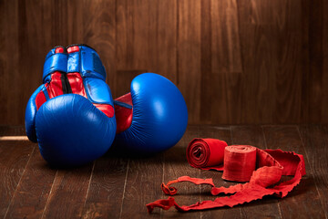 Blue and red boxing gloves with two rolls of hand bandage on wooden background.