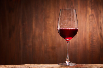 Fragile goblet of the red wine on the wooden stand on wooden wall background.