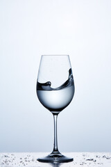 Transparent water wave in the wineglass while standing on the glass with water bubbles against light background.