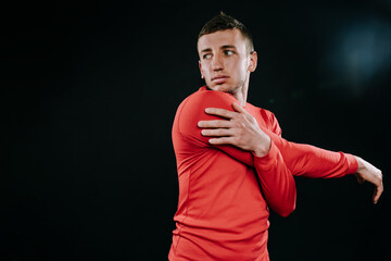 Handsome young European man wearing red sportswear and stretching his arms after a hard workout in dark background. Powerful handsome athletic male doing fit. Sport motivation. Healthy lifestyle.