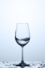 Transparent water wave in the wineglass while standing on the glass with water bubbles against light background.