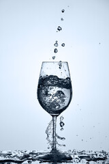 Drinking clean water with water bubbles pouring in wineglass standing on the glass against light background.