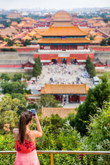 china summer travel. Woman tourist taking pictures with mobile phone of aerial view of imperial palaces, old temples, the forbidden City in Beijing, china. Jingshan Gongyuan park.
