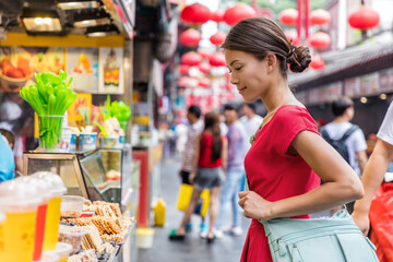 Woman tourist at chinese market Wangfujing, food street on Asia travel. Traditional Beijing snacks at outdoor market place. Asian woman looking at restaurant or outside store.