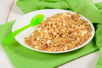 Granola on white plate with green plastic spoon like breakfast for kids
