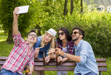 Group of young people taking selfie in the park while eating pizza and drinking beer.