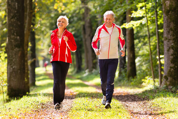 Senior Couple doing sport outdoors, jogging on a forest road in the autumn