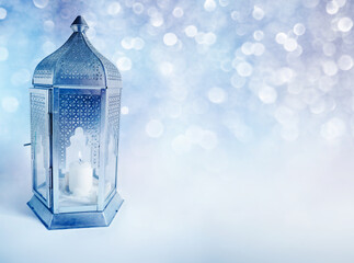 Ornamental Arabic lantern with burning candle glowing at night. Greeting card, invitation for Muslim community holy month Ramadan Kareem. Glittering festive blue background with bokeh lights.