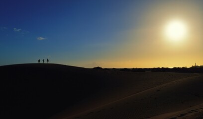 Obraz premium People on the sandy mountain. Sunset in the background.