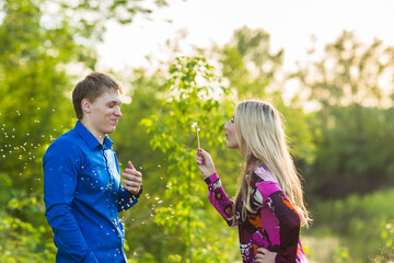 Obraz premium Couple in love blowing blowballs flowers in faces of each other. Smiling and laughing people having good time outside on summer warm day. Woman and man enjoying nature.