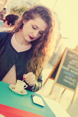 Fototapeta premium Attractive woman holding a cup of coffee at cafe. Close up portrait of cheerful female enjoying street view touriristic road outdoors background. Happiness, leisure and travel vacation lifestyle