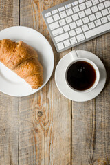Businessman morning with keyboard, cup of coffee and croissant on wooden table background top view mockup