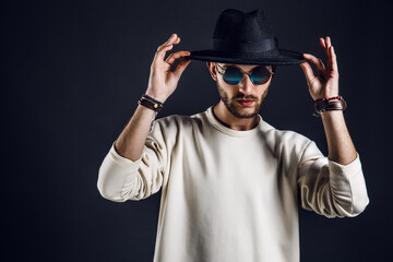 Cool stylish handsome man wearing sunglasses holding hat. Horizontal studio shot.