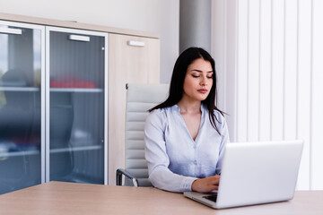 Attractive woman sitting in office and typing on her laptop