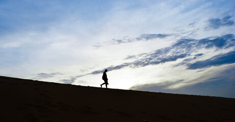 Silhouette man walking down desert  with clouds blue sky background in the morning