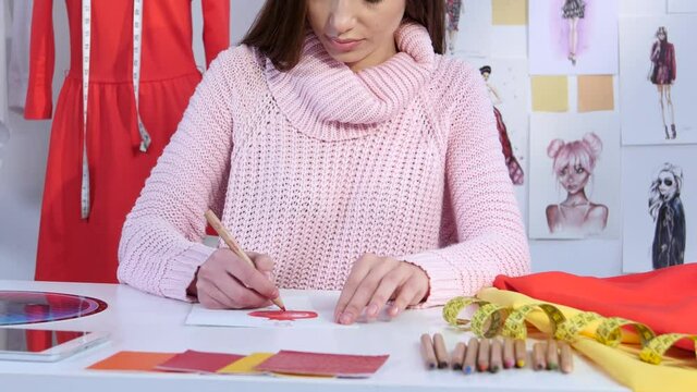 Girl designer draws a sketch of a dress on a table lie fabric samples. Close up
