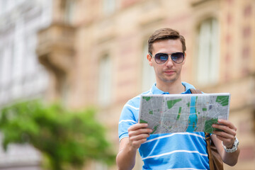 Man tourist with a city map and backpack in Europe street. Caucasian boy looking with map of European city.