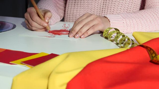 Hands designer draws a sketch of a dress, on a cloth table, for tailoring. Close up