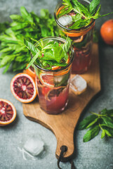 Blood orange citrus lemonade with fresh mint and ice cubes in tall glasses on wooden board over dark brown stone background. Refreshing summer drink concept