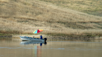 Man fishing on lake with multi-colored umbrella