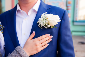 Wedding boutonniere on suit of groom and bride’s hand 